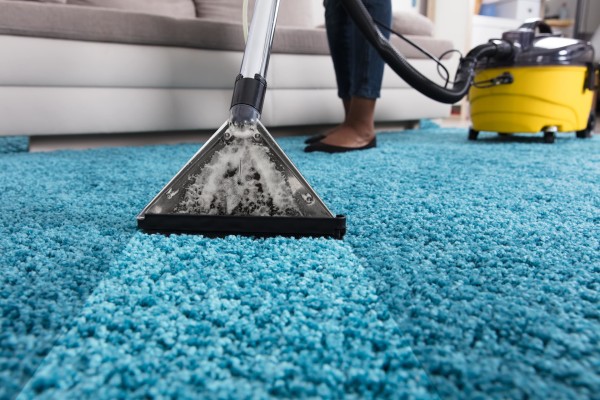 a carpet cleaner is being used on a blue carpet with a focus on the vacuum head and foam and the cleaning unit in the background.jpg
